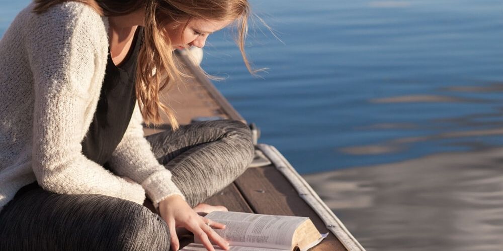 girl sitting on a dock reading her Bible