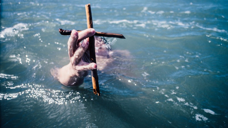 Person underwater holding up small wooden cross above the water