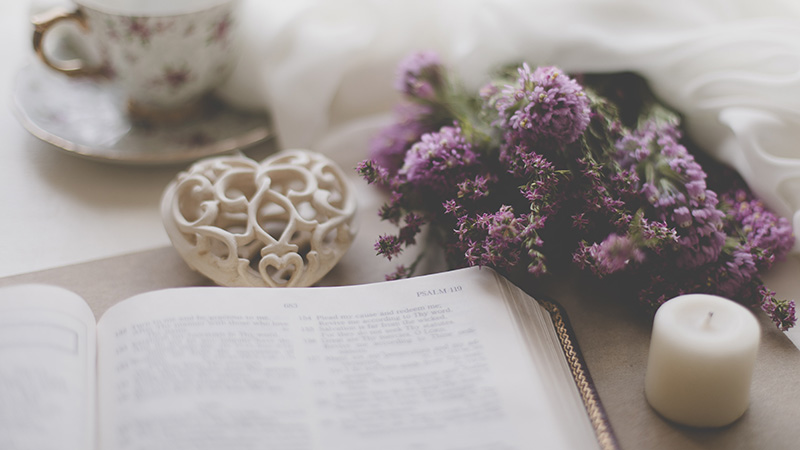 Heart, flowers, candle, and tea next to a bible open to Psalms