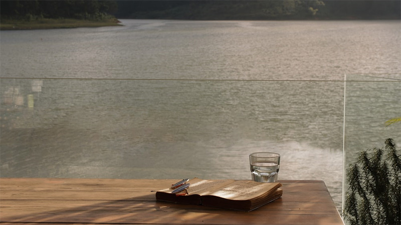 Book on table next to a lake surrounded by forested hills